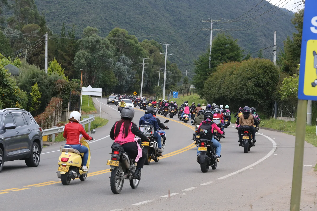 Una larga caravana de motociclistas de La Ruta Rosa, vista desde atrás, recorre una carretera entre montañas