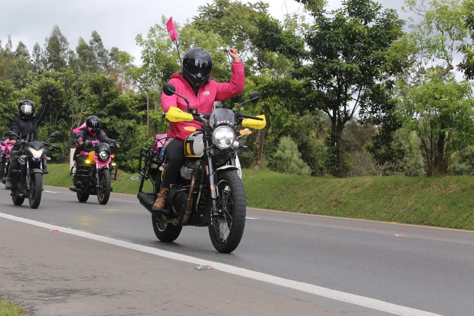 Una participante con chaqueta rosa saluda desde su motocicleta durante la rodada.